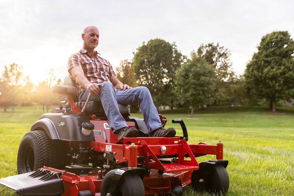 Guy with plaid shirt and jeans Riding Country Clipper Zero Turn mower with Joystick driving option